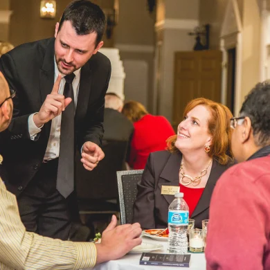 Josh Fletcher performing mentalism at a dinner event, leaning in and pointing while guests smile and react