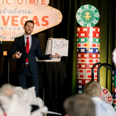 Josh Fletcher mentalist revealing the name Susan on a whiteboard on stage at a Las Vegas-themed corporate event